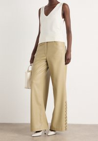 Top senza maniche a collo a V in bianco sporco abbinato a pantaloni larghi in ecopelle beige con dettagli in pizzo all'orlo e décolleté bianche a punta.
