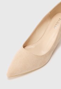Tacón de aguja de ante beige con un diseño de punta afilada. Forro interior suave, que muestra una estética minimalista y detalles de costura limpios.
