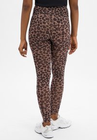 Legginsy w brązowy i czarny wzór panterki z wysokim stanem, wykonane z elastycznego materiału, w zestawieniu z białymi butami sportowymi.