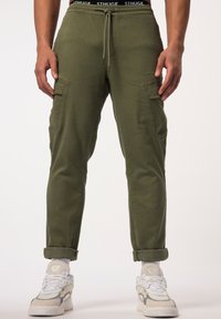 Olijfgroene cargobroek met zijzakken, getailleerde pasvorm, verstelbare tailleband en opgerolde boorden, gecombineerd met wit en grijs sneakers.