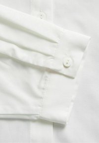 Polsino di camicia bianca con bottoni bianchi, caratterizzato da una texture fresca e liscia. Design sartoriale con una finitura pulita e senza pattern visibili.