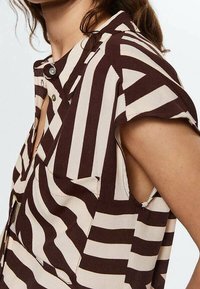Brown and cream striped shirt with short sleeves, featuring a button closure and a slightly loose fit. Textured fabric with side openings.