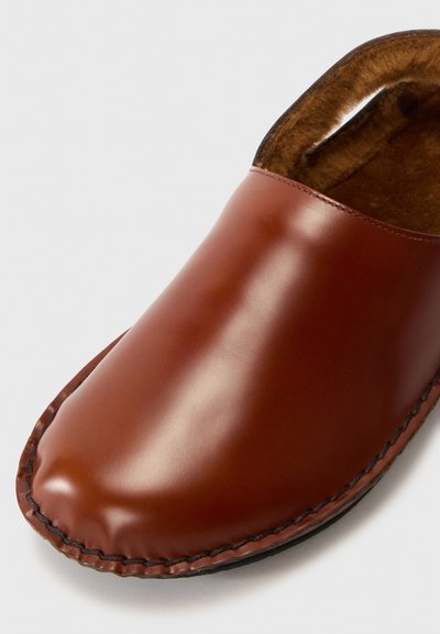 Chaussure en cuir marron à enfiler avec un bout arrondi, surface lisse et coutures contrastées le long de la semelle. Doublée d'un matériau doux.