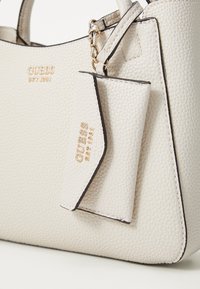 Sac à main en texture de galets blancs avec des accessoires en or, comportant un porte-carte détachable et le nom de la marque embossé sur le devant.