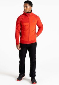 Rote Fleecejacke mit Reißverschluss, Kapuze und schwarzen Akzenten; kombiniert mit schwarzen Hosen und sportlichen schwarzen Schuhen mit roten Sohlen.
