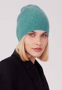 Lichtgroene geribbelde gebreide beanie van zacht materiaal, met een getailleerde vorm en een omgeslagen manchet, gedragen met een zwarte jas.