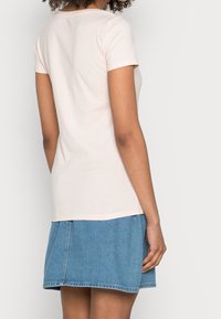 Světle růžové tričko s krátkými rukávy vyrobené z měkké bavlny, doplněné modrou džínovou sukní. Jednoduchý design s klasickým výstřihem a rovného střihu.