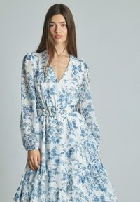 Blumenkleid aus leichtem Stoff, mit blauen Blumenmustern, tiefem V-Ausschnitt, langen Ärmeln, tailliertem Gürtel und gerafftem Saum.