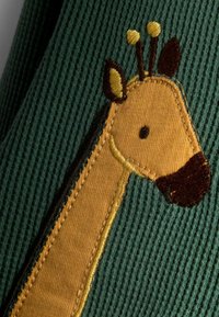 Grønt ribbet stof har et tekstureret, gult og brunt broderet giraffedesign med tydelige ansigtstræk og korte antenner.