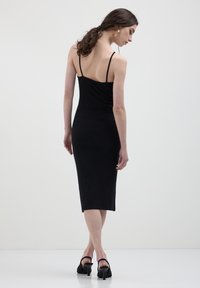 Abito midi nero senza maniche con spalline sottili, design aderente, texture liscia e orlo fino al ginocchio. La vista posteriore mostra una silhouette pulita.