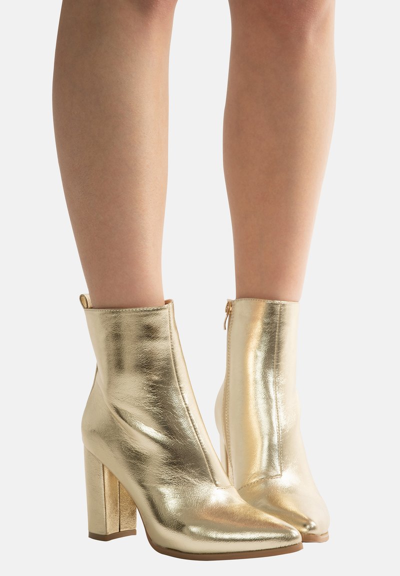 Golden metallic ankle boots with a pointed toe, high block heel, smooth texture, and side zipper detail.
