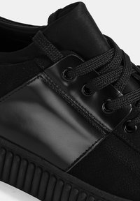 Schwarze Sneaker mit einem strukturierten Stoffobermaterial, glatten Lederakzenten, schwarzen Schnürsenkeln und einer gerippten Sohle für verbesserten Grip.