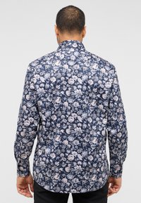 Mørkeblå langærmet skjorte med et blomsterdesign i lyse farver. Glat stof med krave og knapmanchetter.