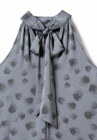 Grau ärmellose Bluse mit dunklen Blumenpunkten und einer gebundenen Schleife am hochgeschlossenen Kragen.