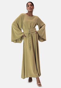 Lungo vestito verde oliva con ampie maniche a campana e vita accentuata. Presenta un dettaglio con lacci in vita e tessuto fluente.