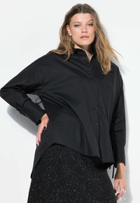 Camicia nera over-size con colletto a punta, maniche lunghe e legacci laterali, abbinata a una gonna nera texturizzata con macchie.