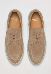 Lichtbruine suède schoenen met een ronde neus, vetersluiting en witte rubberen zool. Voorzien van stikseldetails en branding aan de binnenzijde.