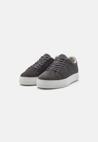 Zapatillas de ante gris con perfil bajo, suela de goma blanca plana y cordones a juego. Textura suave y diseño minimalista con detalles cosidos.