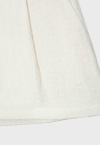 Tissu en lin léger de couleur blanc cassé avec une texture visible et des plis naturels sur un fond clair.