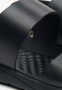 Czarne klapki z gładkiej skóry, z wyprofilowanym wnętrzem stopy i teksturowanymi detalami, oraz subtelnym srebrnym akcentem przy pasku.