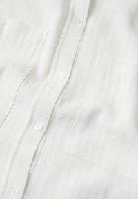 Camisa blanca de botones hecha de un tejido ligero con una sutil textura de rayas verticales, con botones transparentes y un único bolsillo en el pecho.