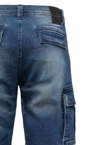 Denim cargo pants featuring a deep blue color, a textured finish, multiple pockets, and a leather label at the waistband.
