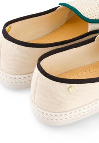Beige canvas instap schoenen met zwarte accenten, voorzien van een textuur inlegzool en een rubberen zool met geweven details. Geaccentueerd met een gouden logo.
