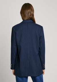 Blazer a rayas con fondo marino y silueta entallada, con cuello de muesca, mangas largas y acentos de botones dorados en los puños.