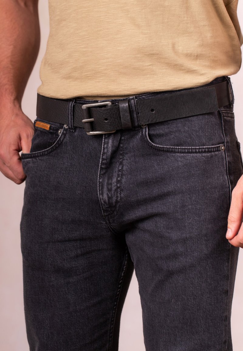 Black leather belt with a rectangular silver metal buckle, worn over dark denim jeans. The fabric is textured, displaying a faded wash.