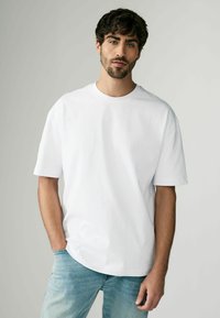 Tricou alb cu mânecă scurtă, cu un guler rotund, realizat dintr-un material fin, asortat cu blugi decolorati, de un albastru deschis, cu o croială casual.