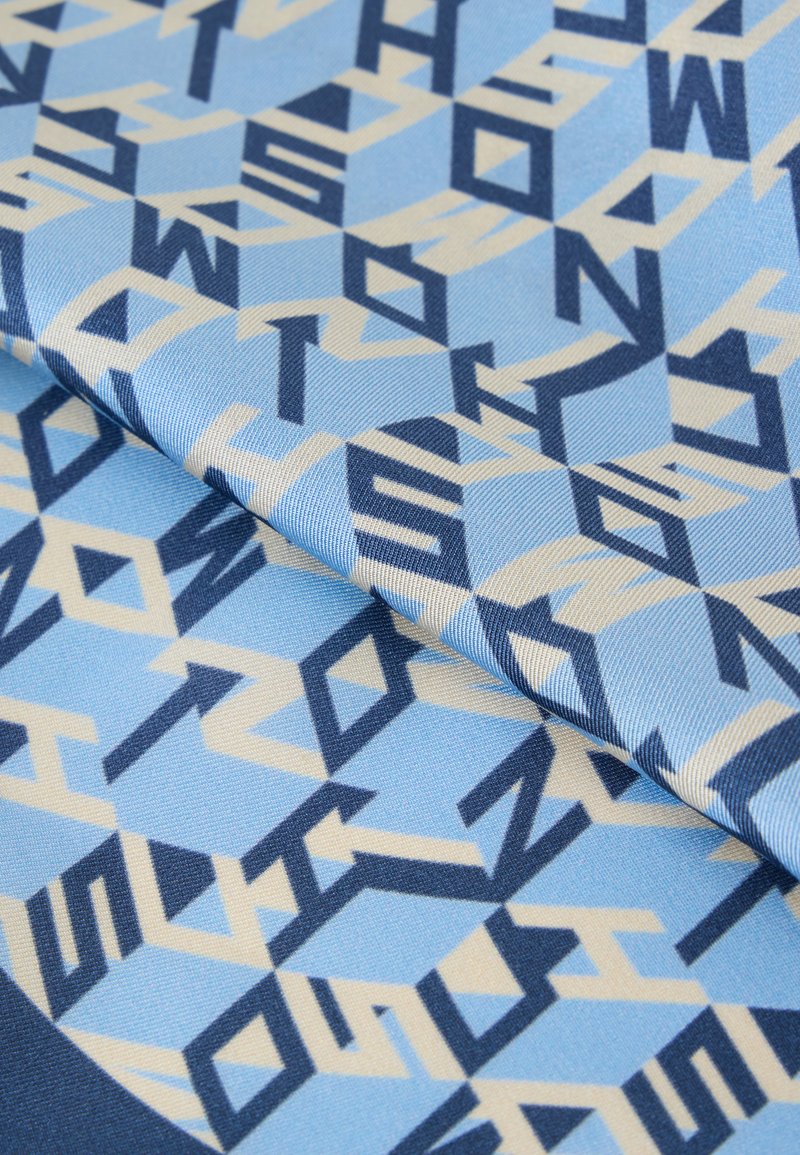Tela azul con un patrón geométrico de letras azules oscuras y claras superpuestas que forman formas de diamante, doblada para mostrar textura y profundidad.