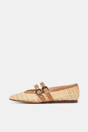 Beiger, spitz zulaufender, geflochtener flacher Schuh mit zwei braunen Lederriemen und goldenen Schnallen vor weißem Hintergrund.