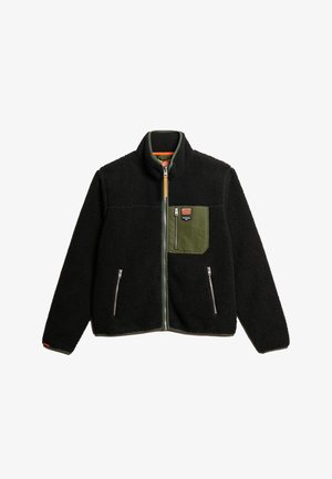 Chaqueta de forro polar negra con un bolsillo verde, cierre de cremallera en la parte delantera y dos bolsillos laterales con cremallera. Presenta un cuello alto y un forro interior en contraste.