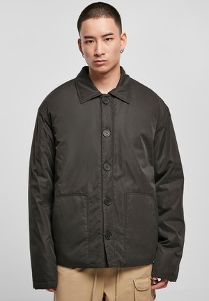 Black, lightweight jacket with a point collar, front button closure, and two side pockets. Smooth texture, boxy shape, casual design.