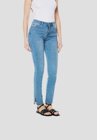 Lichtblauwe strakke jeans met een distressed zoom, subtiele versieringen en een hoog getailleerd ontwerp. Gecombineerd met zwarte sandalen met bandjes.