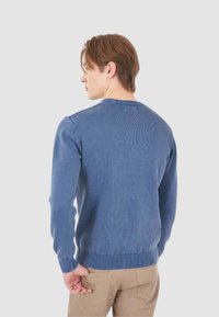 Maglione blu lavorato a maglia con scollatura tonda, polsini e orlo a coste, texture liscia e forma aderente, visto da dietro.