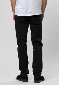 Blugi negri din denim cu croi drept, având două buzunare la spate, purtați cu un tricou alb și pantofi negri.