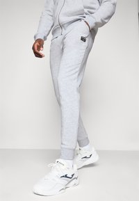 Grå sweatpants lavet af blødt materiale, med en slim fit, ribbede manchetter og sidelommer. Sammen med hvide sportssko.
