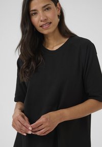 Sort oversized T-shirt med korte raglanærmer, rund halsudskæring og blød stofstruktur. Modellen har langt, mørkt hår. Guld hoopsøreringe.