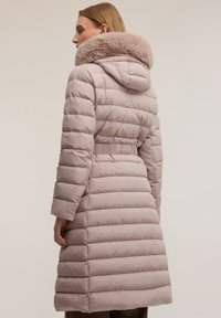 Světle růžový prošívaný kabát s plyšovou odnímatelnou kapucí lemovanou kožešinou, páskem v pase a žebrovanými manžetami. Celý kabát má horizontální prošívaný vzor.
