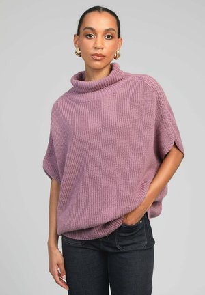 Pull oversize en maille lavande douce avec un col montant à col bénitier et des manches courtes, associé à un jean en denim foncé. Texture, coupe décontractée.