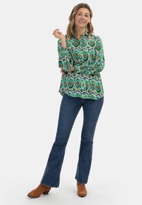 Žalia bluzonė su sudėtingu daugiaspalviu raštu, derinama su platėjančiais mėlynais džinsais ir rudomis suknelėmis su aukšta pakulne. Aprangoje yra apykaklė ir sagų uždarymas.