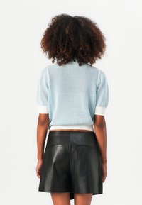 Himmelblaues Netz-Pullover mit kurzen Ärmeln und einem weißen gerippten Saum, kombiniert mit einem schwarzen Leder-A-Linien-Rock mit hinteren Taschen.