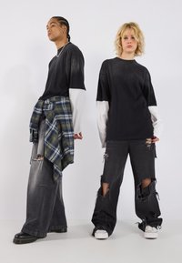 Schwarze übergroße T-Shirts mit kontrastierenden langen weißen Ärmeln, distressed schwarze Jeans und ein kariertes Flanellhemd um die Taille gebunden. Klobiges Schuhwerk.
