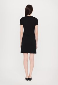 Μαύρο φόρεμα κοντό μανίκι, μέχρι το γόνατο, φτιαγμένο από μαλακό ύφασμα, με στρογγυλή λαιμόκοψη και ίσια γραμμή. Λείο υλικό, μινιμαλιστικός σχεδιασμός.
