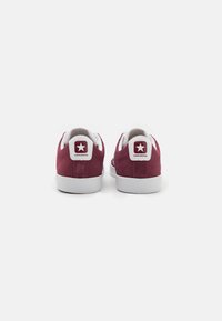 Burgundy suede sneakers with white rubber soles and tongue, featuring a red star logo on the heel and contrasting white accents.