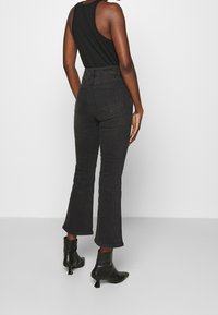 Jeans neri a vita alta e svasati, con una vestibilità slim sulle cosce. Presentano tasche posteriori e un tessuto testurizzato. Abbinati a stivali neri con tacco alla caviglia.