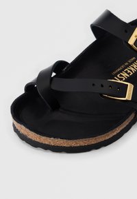 Μαύρο δερμάτινο σανδάλι Birkenstock με φελλό πάτο, ρυθμιζόμενο λουρί με χρυσή αγκράφα και ανάγλυφη σόλα σε ανοιχτό φόντο.