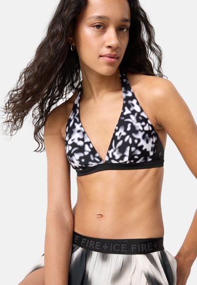 Ung kvinde med langt krøllet hår iført sort og hvidt mønstret halter-bikini top og matchende nederdel med "FIRE + ICE" taljebånd.