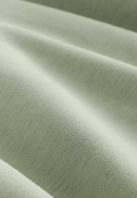 Tissu lisse vert clair avec des plis doux et une texture fine tissée, présenté en détail rapproché.